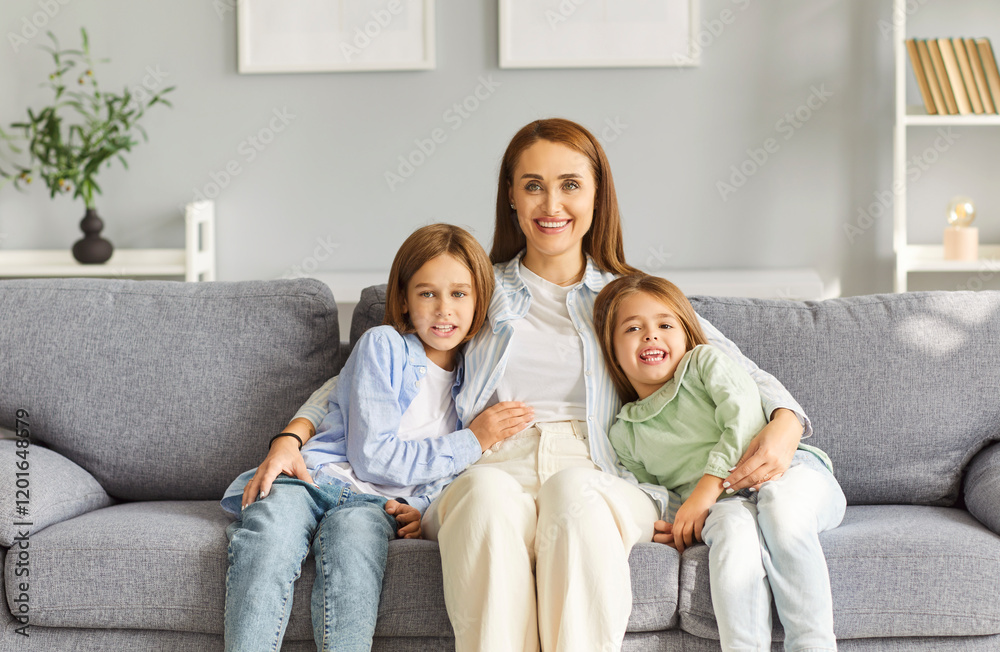Happy smiling bonding family, mother with two adorable small kids siblings looking at camera, laughing having good time, fun, care at home together on soft sofa, feel comfortable, safe indoors Happy smiling bonding family, mother with two adorable small kids siblings looking at camera, laughing having good time, fun, care at home together on soft sofa, feel comfortable, safe indoors
