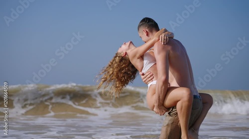 Happy married couple playing in the ocean. Woman jumps to the man, husband spinning his wife in the sea near paradise island. Slim boyfriend and girlfriend enjoying romantic vacation at the resort.