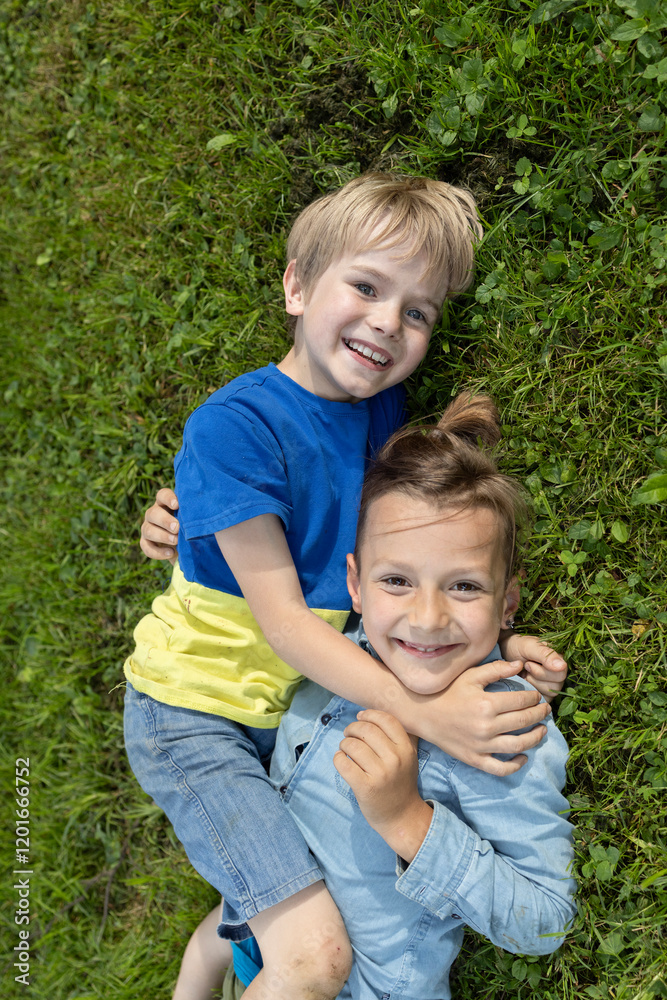 Two cheerful boys are lying on grass, hugging each other. concept of friendship, happy relationship between brothers. Active recreation in park or in school yard. positive, joy of childhood. Top view Two cheerful boys are lying on grass, hugging each other. concept of friendship, happy relationship between brothers. Active recreation in park or in school yard. positive, joy of childhood. Top view