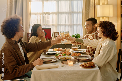 Wide shot of biracial friends sitting at festive table with a lot of plates with homemade delicious food and clinking glasses with apple juice
