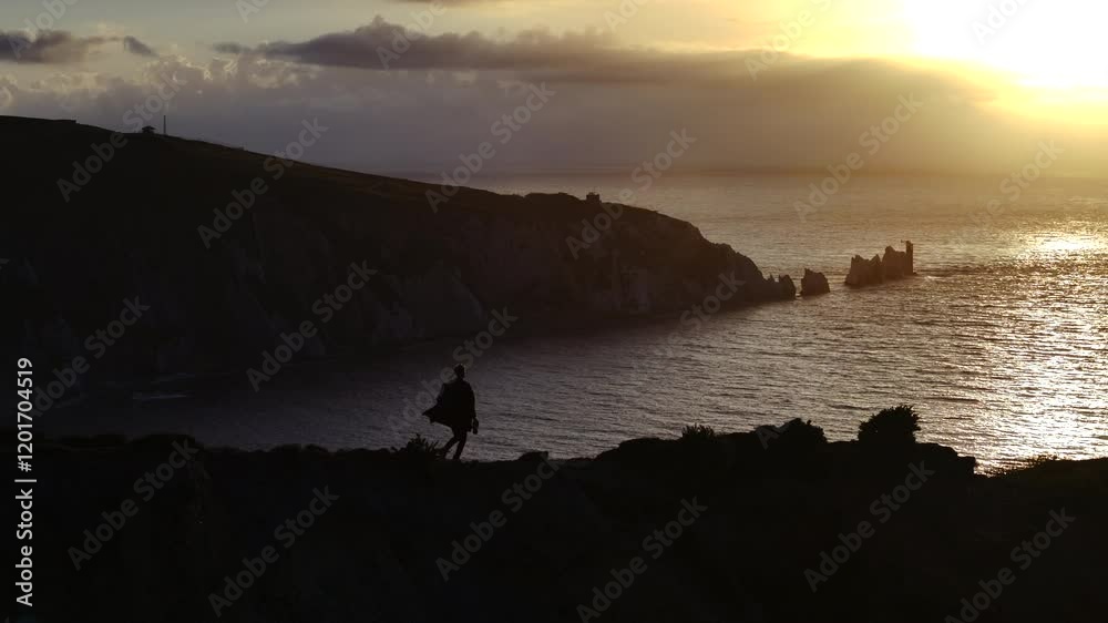 A man is walking on a beach at sunset. The sky is orange and the water is calm