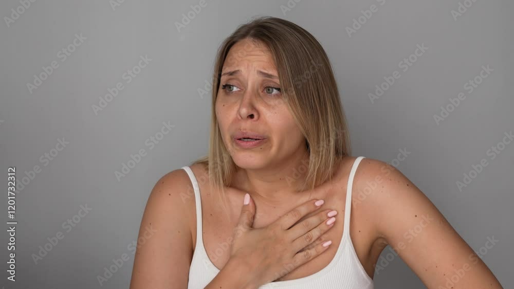 Young blonde woman holding the chest with her hands suffering from panic attack on a grey background. Heartburn, pain, acid reflux, indigestion, osteochondrosis, neurological diseases. Chest tightness Young blonde woman holding the chest with her hands suffering from panic attack on a grey background. Heartburn, pain, acid reflux, indigestion, osteochondrosis, neurological diseases. Chest tightness