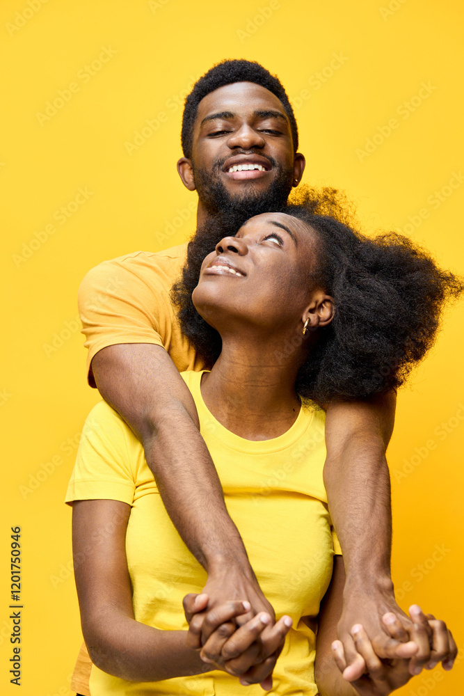 Obraz premium Happy young African couple embracing against a vibrant yellow background, showcasing love and joy in matching outfits, ideal for romantic and lifestyle themes
