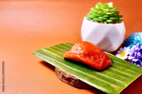 Kue angku ketan kacang ijo with plants display on the back. Chewy glutinous rice cake dish. Indonesian traditional jajanan pasar dessert snacks isolated on horizontal copy spaced orange background. photo