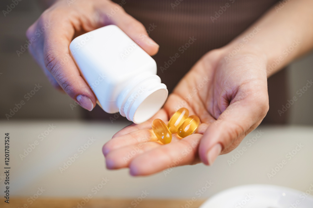 Athletic woman in sportswear is holding omega-3 capsules, fish oil supplements in her hand, in a kitchen Athletic woman in sportswear is holding omega-3 capsules, fish oil supplements in her hand, in a kitchen