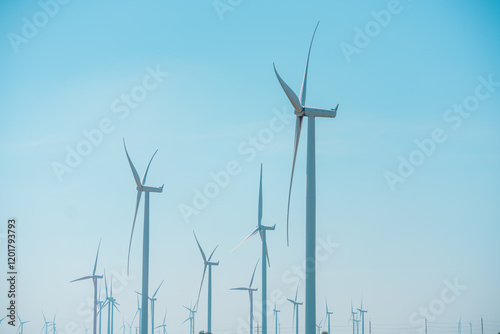 Large wind turbines standing tall against a clear blue sky in a renewable energy field during daylight hours photo