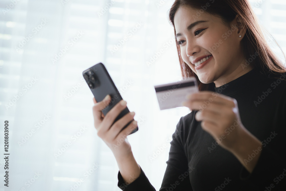 Young Asian woman smiling while using smartphone and holding credit card to buy things online. Image highlights e-commerce, finance, technology and convenience of digital transactions. Young Asian woman smiling while using smartphone and holding credit card to buy things online. Image highlights e-commerce, finance, technology and convenience of digital transactions.