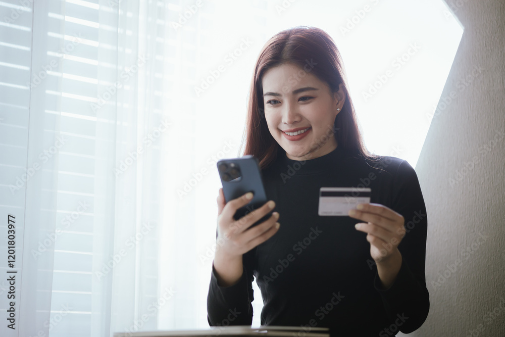 Young Asian woman smiling while using smartphone and holding credit card to buy things online. Image highlights e-commerce, finance, technology and convenience of digital transactions. Young Asian woman smiling while using smartphone and holding credit card to buy things online. Image highlights e-commerce, finance, technology and convenience of digital transactions.