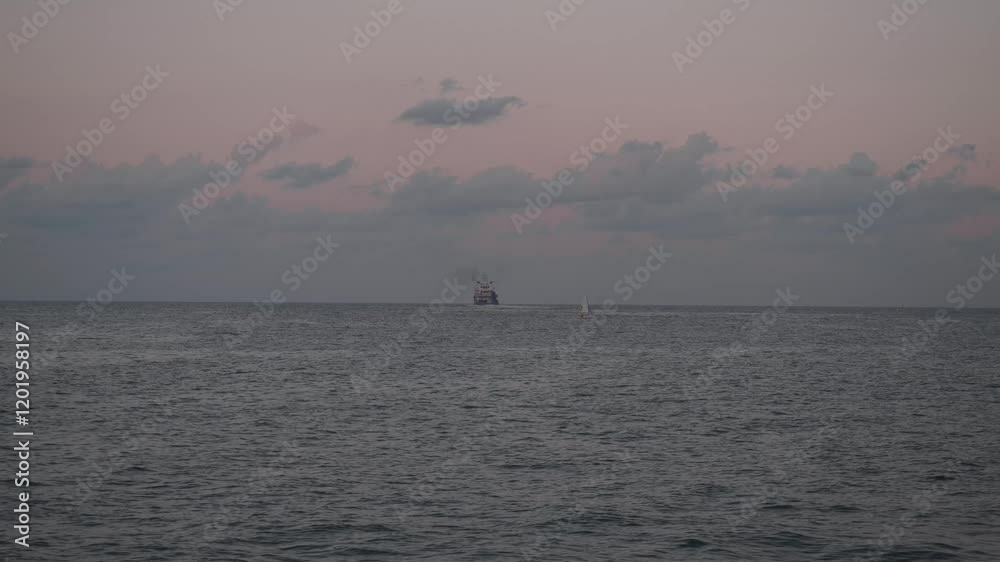 The Serene and Beautiful Sunset Over a Calm Ocean with a Ship Sailing on the Distant Horizon The Serene and Beautiful Sunset Over a Calm Ocean with a Ship Sailing on the Distant Horizon