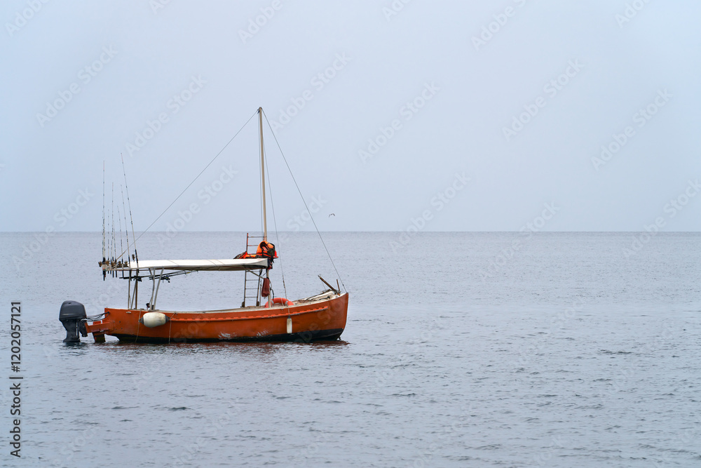 Fototapeta premium Fishing tourism. Sea fishing at a distance from the shore. A lone motorboat with a set of fishing rods on board is anchored in a sea bay. Copy space.
