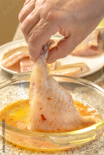 Chef dips a piece of fish into liaison - a mixture of raw eggs, salt, paprika before frying