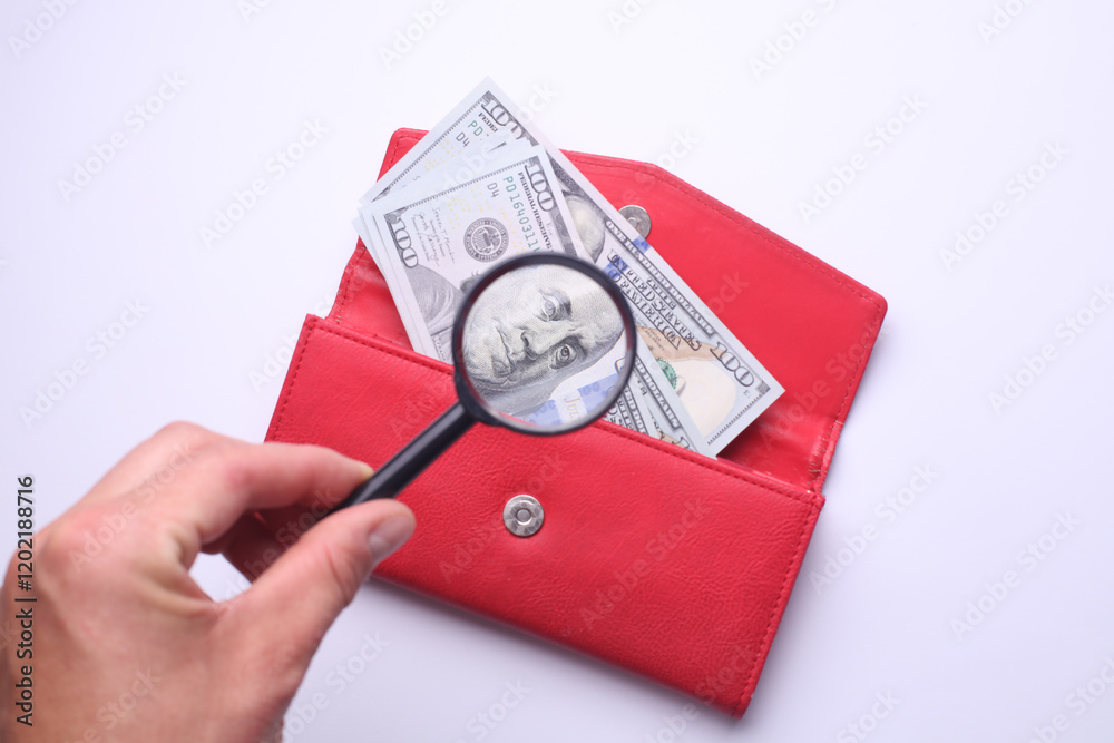 Hand with magnifying glass looks at dollars in wallet Hand with magnifying glass looks at dollars in wallet