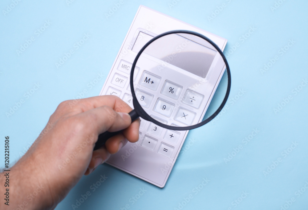 Hand with a magnifying glass examines calculator on blue background