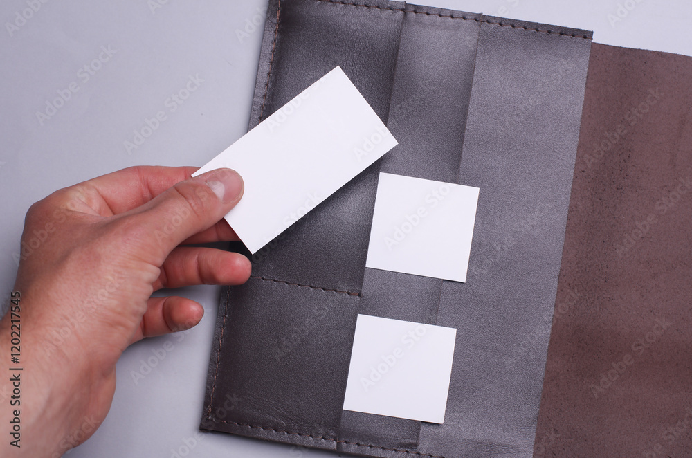 Fototapeta premium Hand taking white business card from leather business card holder on grey background