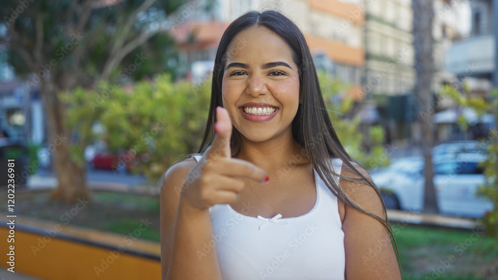 Woman smiling in outdoor urban park pointing at camera with confidence capturing the essence of youthful, lively, and attractive hispanic presence in a vibrant city setting. Woman smiling in outdoor urban park pointing at camera with confidence capturing the essence of youthful, lively, and attractive hispanic presence in a vibrant city setting.