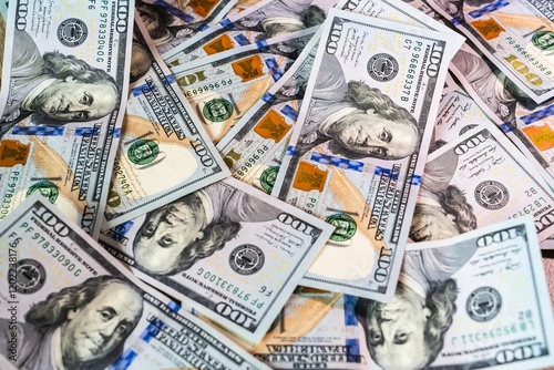 Stacks of hundred dollar bills spread across a surface in a casual array on a bright background