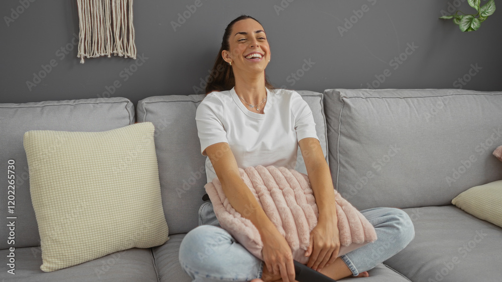 Woman sitting on gray couch smiling holding pillow in urban home interior Woman sitting on gray couch smiling holding pillow in urban home interior
