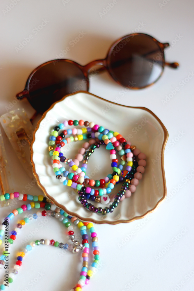 Hand figurine, sunglasses, gold jewelry, colorful bead jewelry, statement rings and various hair accessories on the white table. Selective focus.
