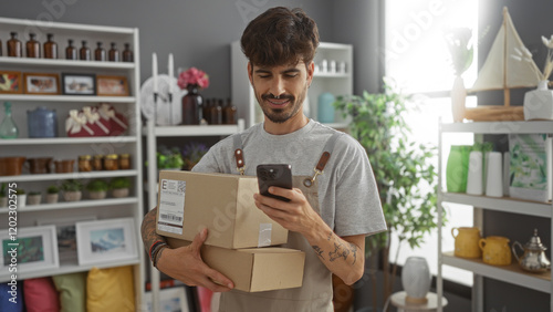 Quadro em tela Handsome young man with a beard checking his mobile phone while holding packages