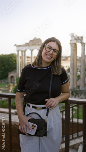 Canvas Print Woman smiling in rome with the roman forum in the background holding a phone, wearing glasses, standing outside, showcasing hispanic heritage in a historic european setting