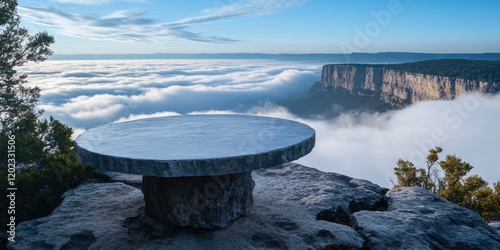 A round stone table is placed on the edge of mountain cliff, sunny sky on background