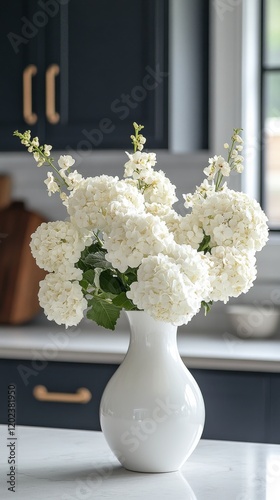 Beautiful white hydrangeas arranged in a vase on a kitchen countertop with mo...