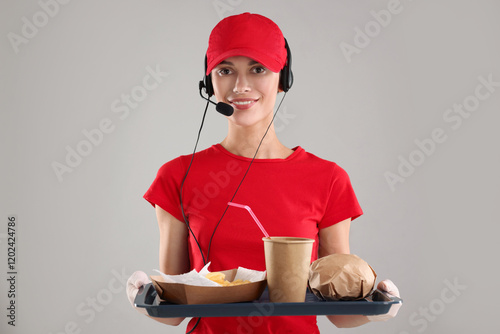 Fast-food worker holding tray with order on gray background, photo