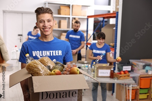 Volunteer holding donation box with food products indoors, selective focus photo