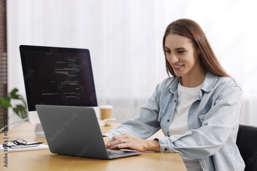 Programmer working on laptop and computer at wooden desk indoors Programmer working on laptop and computer at wooden desk indoors