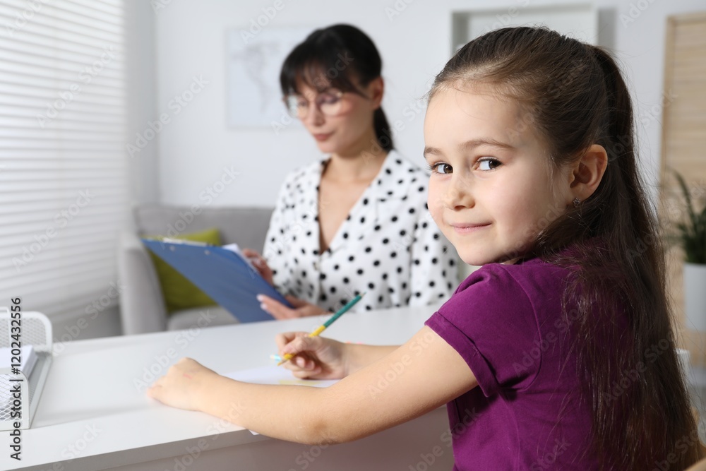 Little girl drawing at desk while psychologist taking notes, selective focus Little girl drawing at desk while psychologist taking notes, selective focus