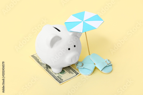 Piggy bank with money and beach accessories on pale yellow background. Concept of savings for travel