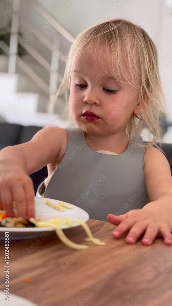 Cute toddler enjoys meal at home, showcasing playful eating habits while seated Cute toddler enjoys meal at home, showcasing playful eating habits while seated