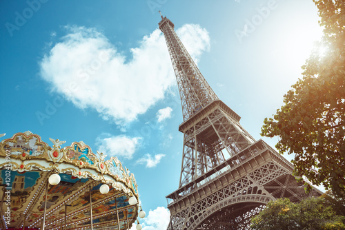 Vivid view of the Eiffel Tower with a charming carousel in the foreground, framed by lush greenery and a bright sunny sky. Perfect for travel, tourism, and cultural projects.