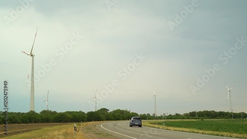 a road with a passing car past wind turbines