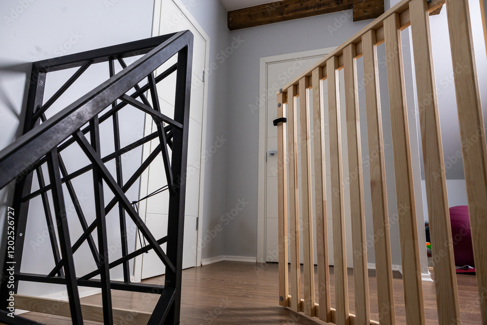 Indoor space featuring a black metal staircase, light wooden gate, polished wood floor, gray walls, white doors, and a wooden ceiling beam. Indoor space featuring a black metal staircase, light wooden gate, polished wood floor, gray walls, white doors, and a wooden ceiling beam.