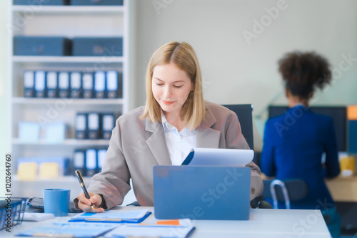 A young Russian woman in formal suit works diligently in business office, analyzing financial charts, using a desktop PC, calculator while contributing to various business strategies and projects.