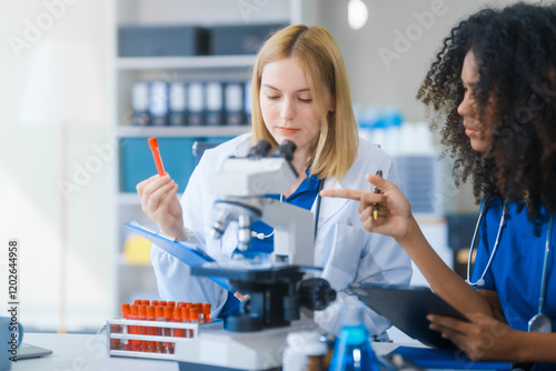 Young African American and Russian woman, both scientists, collaborate to analyze blood samples, viruses, vaccines using microscopes. They conduct crucial medical and biological research.