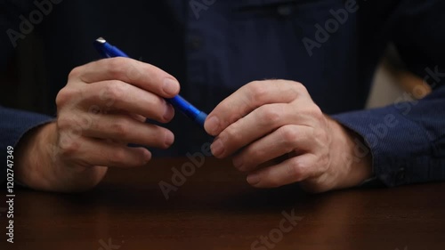 male hands nervously twirl a ballpoint with their fingers. man thoughtfully or nervously or frustratedly fiddles with a blue ballpoint pen with his hands. close-up. photo