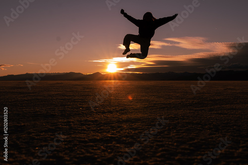 A person doing a heel kick at the Salt Flats with a sunset going over the mountains in the horizon