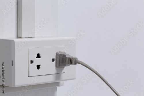 Plug from an electrical appliance. plugged into an electrical outlet on white wall background.