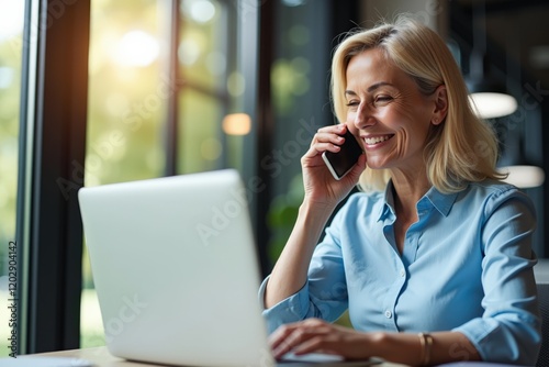 Smiling Businesswoman on Phone While Working on Laptop in Modern Office Environment with Natural Light and Green View Outside