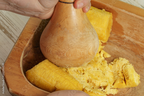 Wooden mortar mashing boiled plantains in a rustic bowl, showing the second step in the preparation of mashed green plantain, a tropical dish that holds cultural, culinary and traditional significance photo