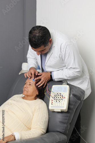 Elderly Latin woman undergoes EEG electroencephalogram to detect dementia or Alzheimer's disease in office with dark-skinned specialist doctor