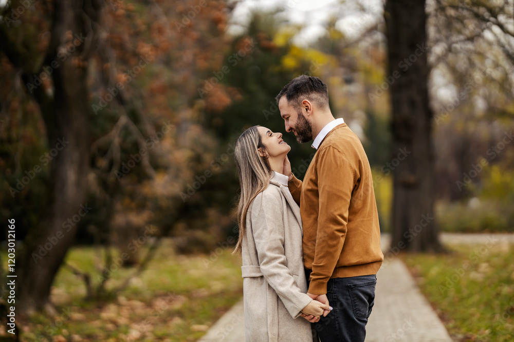 Side view of affectionate couple in love holding hands and looking at each other in city park. Side view of affectionate couple in love holding hands and looking at each other in city park.