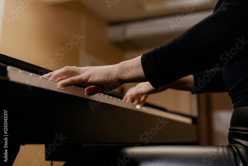 Close up view of gentle female hands with small ring in black clothes playing piano her favorite classical music, learning new melody, taking lessons. Romantic beige subdued light. Bottom view photo