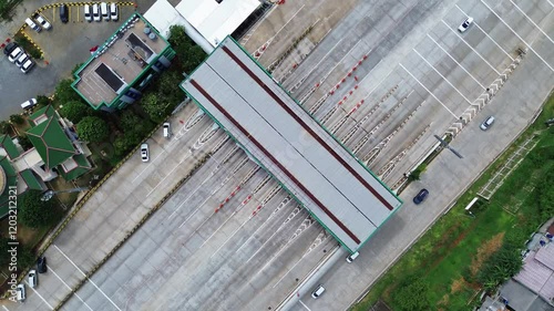 Overhead drone shot of a highway toll booth with cars entering and exiting. Clear view of lanes and infrastructure.