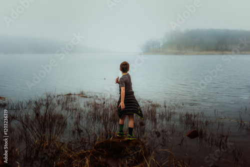 Boy skipping rocks on a foggy lake