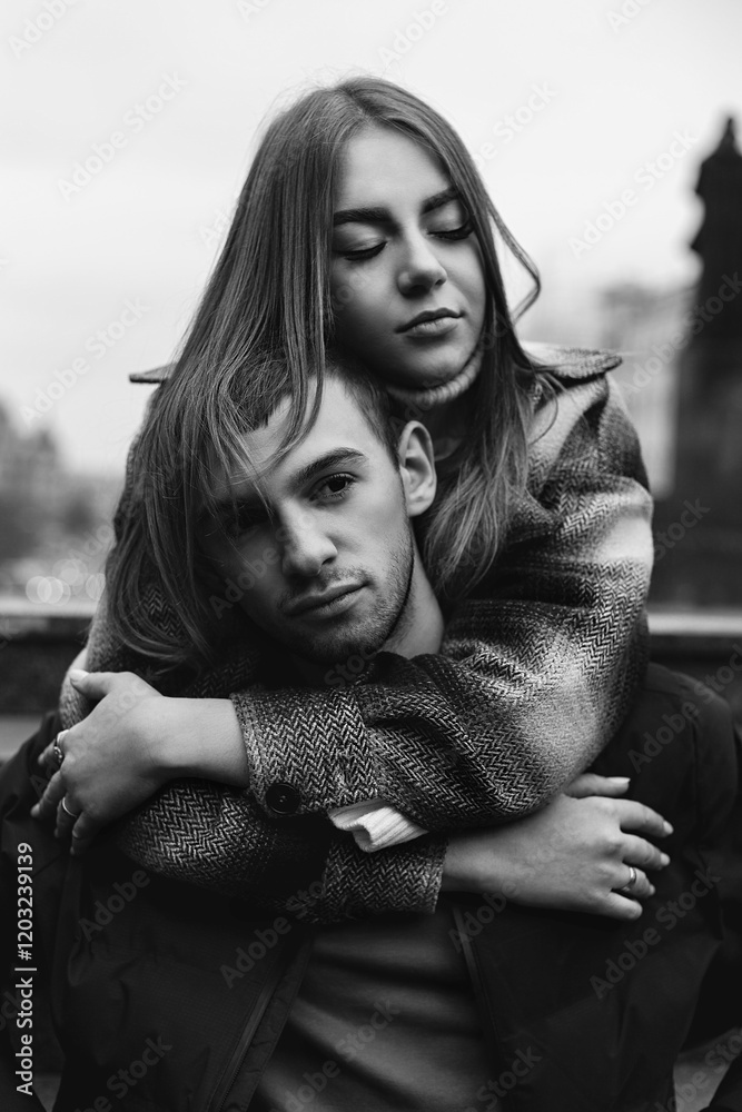 two young people. The girl hugs the guy from behind, putting her hands on his shoulders. She has long hair and closed eyes and looks relaxed. The guy looks straight into the camera two young people. The girl hugs the guy from behind, putting her hands on his shoulders. She has long hair and closed eyes and looks relaxed. The guy looks straight into the camera