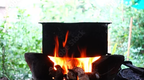 In a simple and old-fashioned way, cooking food with a stainless steel pot and an Anglo charcoal stove. to get a dark sooty color over a long time. The charcoal stove has a red light on it.
