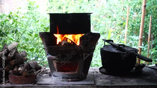 In a simple and old-fashioned way, cooking food with a stainless steel pot and an Anglo charcoal stove. to get a dark sooty color over a long time. The charcoal stove has a red light on it.